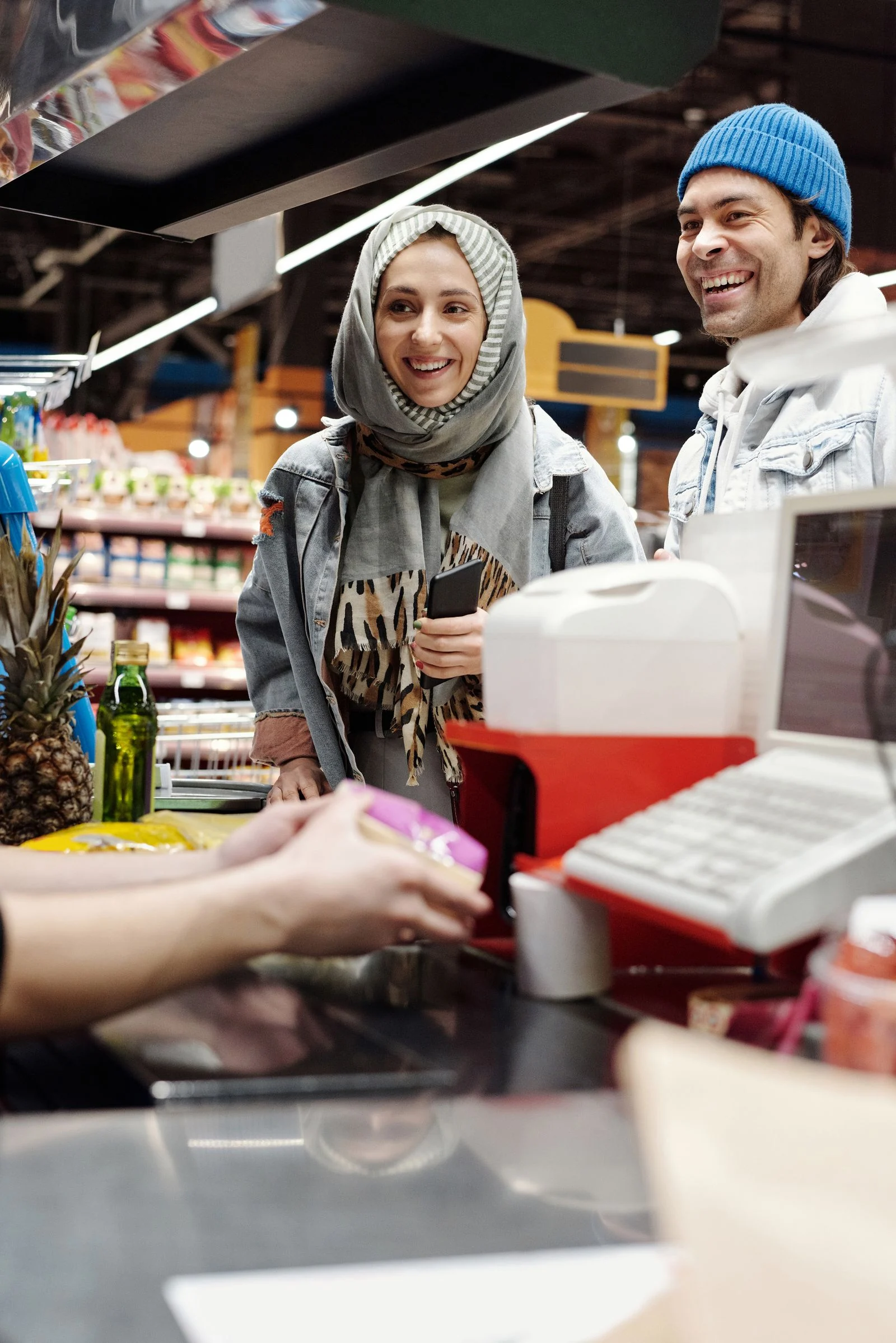 Customers and a shop assistant interacting at a supermarket checkout.